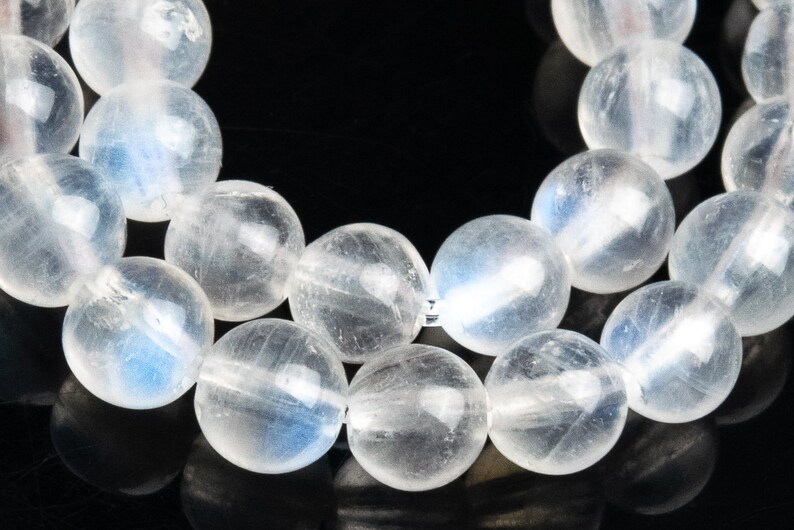 May include: A strand of white moonstone beads. The beads are round and smooth, with a slight iridescent sheen.
