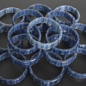 May include: A pile of blue gemstone bracelets made of rectangular beads. The bracelets are stacked on top of each other, creating a circular pattern.
