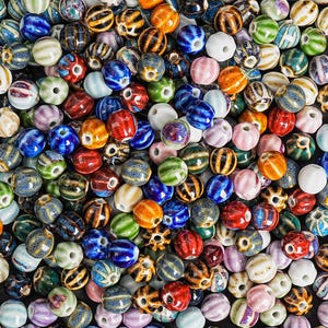 Könnte beinhalten: Eine große Sammlung bunter Keramikperlen in verschiedenen Formen und Mustern. Die Perlen sind eine Mischung aus Blau, Grün, Rot, Weiß und Braun.