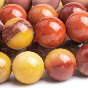 May include: A strand of round, polished gemstone beads in shades of red, orange, and yellow. The beads are smooth and have a natural, earthy look.