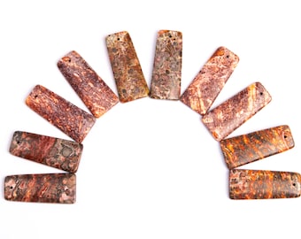 Puede incluir: Un conjunto de diez colgantes rectangulares de piedra de ágata marrón y naranja con un agujero en la parte superior. Las piedras tienen un patrón de mármol.