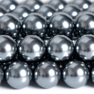 May include: Close-up of numerous, evenly spaced, dark gray, spherical beads. The beads have a glossy, reflective surface, with highlights creating a sense of depth. The arrangement suggests a craft supply or jewelry component.