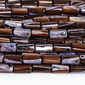 May include: Close-up of a collection of rectangular beads in shades of brown and purple. The beads have a glossy finish and are arranged closely together, creating a textured surface. The beads are likely for jewelry making.