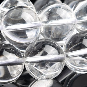 Puede incluir: Primer plano de una hebra de cuentas de cuarzo transparente con un hilo blanco que atraviesa el centro de cada cuenta.