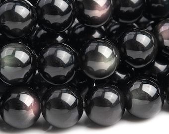 May include: A close-up of a collection of polished, round, black obsidian beads. The beads have a glossy, reflective surface, with subtle variations in color and sheen. The beads are arranged closely together, filling the frame.