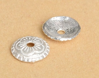 May include: Two silver-toned metal bead caps with a decorative design. One cap has a smooth surface, while the other has a floral pattern.