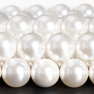May include: Close-up of lustrous, white pearls arranged in neat rows. The spherical beads reflect light, creating a soft, elegant appearance. The pearls are a classic accessory, often used in jewelry.