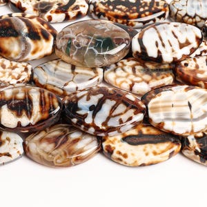 May include: A collection of oval-shaped fire agate beads featuring a polished finish. Each bead displays a unique pattern of dark brown, cream, and translucent white veins, creating a marbled appearance with smooth, rounded edges throughout.