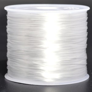 Könnte beinhalten: Eine Spule mit durchsichtigem elastischem Garn, das fest auf einer weißen Kunststoffspule gewickelt ist.