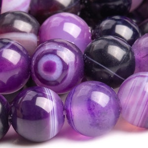 May include: A strand of purple agate beads with white and black banding. The beads are round and smooth, and they have a polished finish.