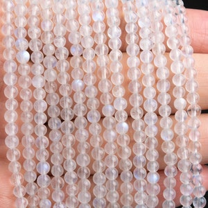 May include: A strand of white moonstone beads, each bead is round and smooth. The beads are strung on a clear thread and are arranged in a straight line. The beads are translucent and have a slight iridescent sheen.