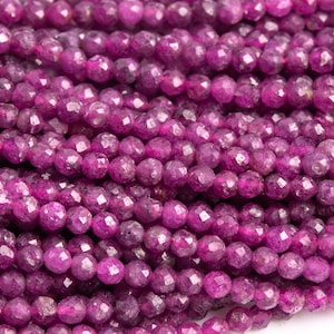 May include: Close-up of strands of faceted, deep magenta-colored gemstone beads. The beads are small, round, and strung together, creating a textured surface. These beads are suitable for jewelry making.