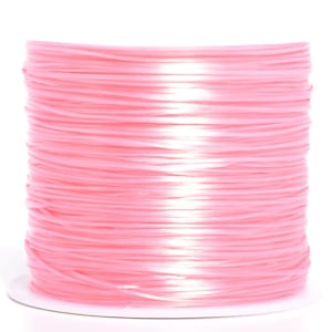 May include: A spool of light pink raffia ribbon. The ribbon is tightly wound, creating a cylindrical shape. The color is a soft, pastel pink, and the ribbon appears to be made of a smooth, slightly shiny material. The spool sits on a white base.