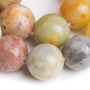 May include: A strand of round, smooth, multi-colored gemstone beads. The beads are various shades of green, brown, gray, and yellow.