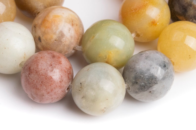 May include: A strand of round, smooth, multi-colored gemstone beads. The beads are various shades of green, brown, gray, and yellow.
