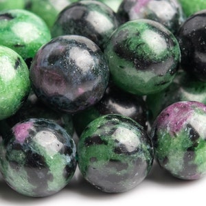 Peut inclure: Un ensemble de perles de pierres précieuses polies. Les perles sont sphériques, avec un mélange de teintes vertes, noires et violettes. Les pierres précieuses ont une finition brillante, et les couleurs sont tourbillonnées et mouchetées dans les pierres. Les perles sont probablement destinées à la fabrication de bijoux.