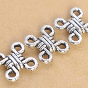 May include: Three silver metal decorative charms in the shape of a knot. The charms are intricately designed and have a polished finish.