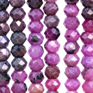 May include: A strand of faceted gemstone beads in shades of purple and pink. The beads are round and have a faceted finish.