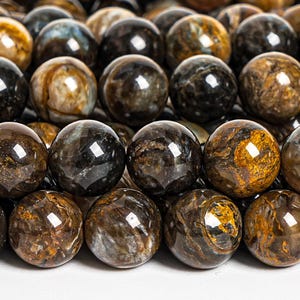 Può includere: Primo piano di una collana di perle rotonde in pietre preziose marroni, nere e dorate. Le perle hanno una qualità scintillante e iridescente.