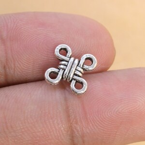 May include: Silver metal charm with a knot design. The charm is shaped like a cross with four loops.