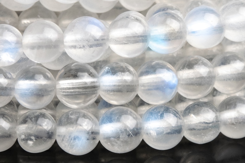 May include: A strand of white moonstone beads, each bead is round and smooth with a slight iridescent shimmer.