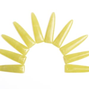 May include: A collection of ten pale yellow, elongated, pointed objects arranged in a semi-circle against a white background. Each object has a flat, rectangular base and tapers to a rounded point. The objects appear to be made of a smooth, solid material.