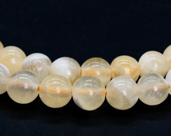 Könnte beinhalten: Eine Kette aus großen, runden Perlen in Creme- und Hellgelbtönen. Die durchscheinenden Perlen weisen subtile Farbvariationen und innere Muster auf. Die Perlen sind mit einem gelben Faden aufgereiht, geeignet für die Schmuckherstellung.
