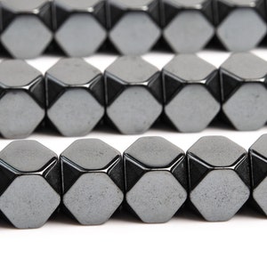 May include: A strand of black hematite beads with a faceted, hexagonal shape. The beads are arranged in rows and have a slightly metallic sheen.