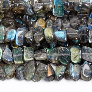 Pode incluir: Close-up de uma coleção de pedras preciosas de labradorita polidas. As pedras exibem uma mistura de tons cinza, azul, verde e dourado. Cada pedra tem uma forma e textura únicas, com uma superfície polida e lisa. As pedras preciosas estão dispostas próximas umas das outras.