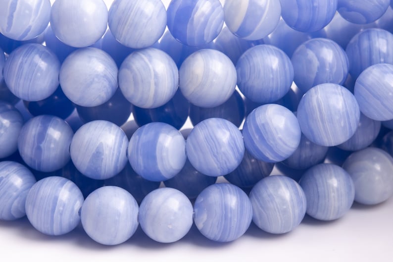 K&ouml;nnte beinhalten: Eine Reihe blauer Achatperlen mit wei&szlig;en Wirbeln. Die Perlen sind rund und glatt und in einer Nahaufnahme angeordnet.