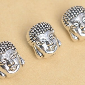 May include: Three silver-toned Buddha head charms with a textured surface. The charms are approximately 1 inch in diameter.
