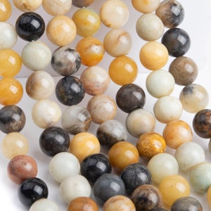 May include: A strand of round, smooth, natural stone beads in shades of yellow, brown, white, and black. The beads are strung on a clear thread.