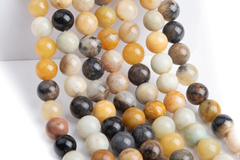 May include: A strand of round, smooth, natural stone beads in shades of yellow, brown, white, and black. The beads are strung on a clear thread.