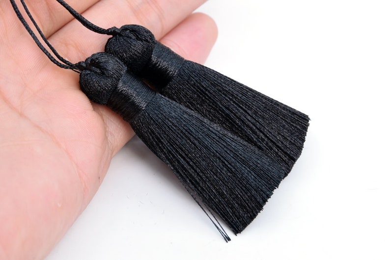 K&ouml;nnte beinhalten: Zwei schwarze Quastenb&auml;nder mit einem Knoten oben. Die Quasten bestehen aus d&uuml;nnen Stofff&auml;den und sind etwa 12,5 cm lang.
