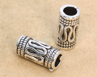 May include: Two silver-coloured cylindrical beads with an intricate design. The beads have a textured surface with a repeating pattern of wavy lines and rope-like details. These beads are likely for jewellery making.