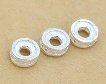 May include: Three silver-toned metal spacer beads with a decorative design around the edge. The beads are round with a hole in the centre.