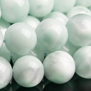 May include: A close-up of a strand of light green, round, smooth beads. The beads have a subtle iridescent sheen.