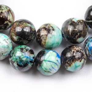 K&ouml;nnte beinhalten: Eine Kette aus runden, schwarzen, gr&uuml;nen und blauen Edelsteinperlen. Die Perlen haben ein marmoriertes Muster und sind auf einem durchsichtigen Faden aufgef&auml;delt.