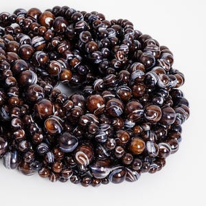May include: A collection of brown and white striped beads of varying sizes. The beads have a glossy finish and are arranged in a dense, organic shape. The beads are likely for jewelry making.