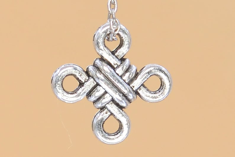 May include: Silver charm with a knot design in the shape of a cross.
