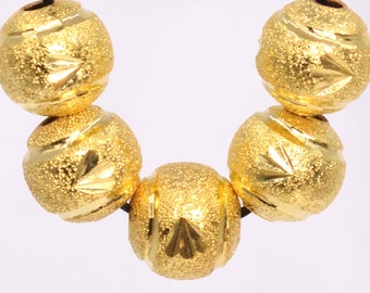 May include: A strand of five gold-colored beads with a textured surface and a decorative design. The beads are round and have a shiny finish.