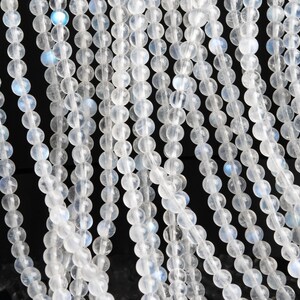 May include: A strand of white moonstone beads, each bead is round and smooth. The beads have a subtle iridescent sheen.
