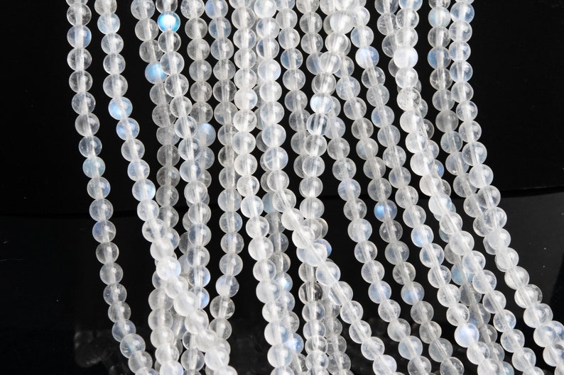 May include: A strand of white moonstone beads, each bead is round and smooth. The beads have a subtle iridescent sheen.