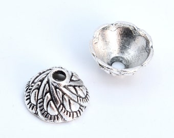 Op de afbeelding: Twee zilveren metalen kralencaps met een versierd ontwerp. De doppen zijn rond en hebben een gat in het midden.