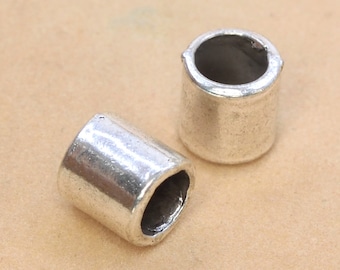 Puede incluir: Dos tapas de cuentas de metal plateado para la elaboración de joyas. Las tapas son cilíndricas y tienen un acabado liso y brillante.