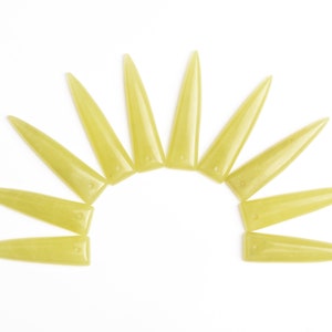 May include: A set of ten yellow nail tips arranged in a semi-circle shape.