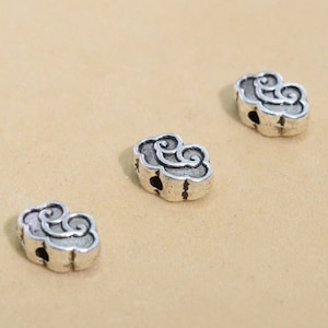 May include: Three silver-colored cloud-shaped beads with a distressed finish. Each bead features a detailed swirling design and a small hole for stringing. The beads are scattered on a neutral-toned surface.