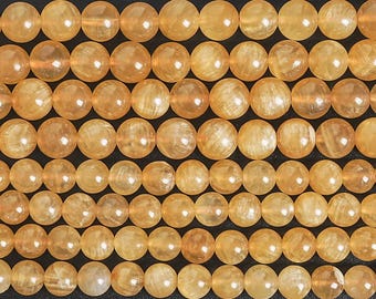 Könnte beinhalten: Nahaufnahme von Reihen goldgelber Edelsteinperlen. Die Perlen sind rund und haben eine durchscheinende Optik mit Farb- und Texturvariationen. Die Perlen sind aufgefädelt und eignen sich ideal für die Schmuckherstellung oder Bastelarbeiten.