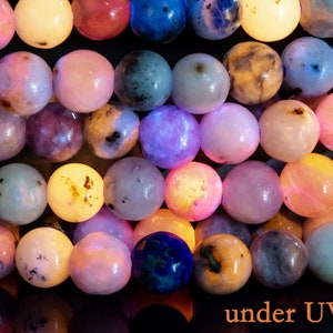 May include: A close-up of a strand of colorful beads under a UV light. The beads are round and smooth, and they glow brightly in different shades of pink, purple, blue, and yellow.