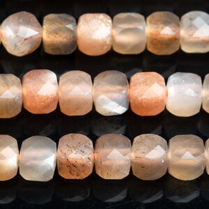 May include: A strand of faceted sunstone beads in shades of peach, orange, and white. The beads are square-shaped and have a smooth, polished finish.
